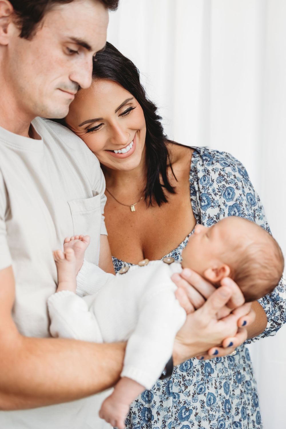 Parents admiring their newborn baby against white curtain background in New Haven, CT.