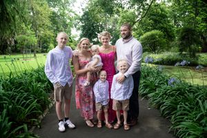 A family of six is posing together in a lush garden. There are two adults and four children The adults are standing in the center, with them