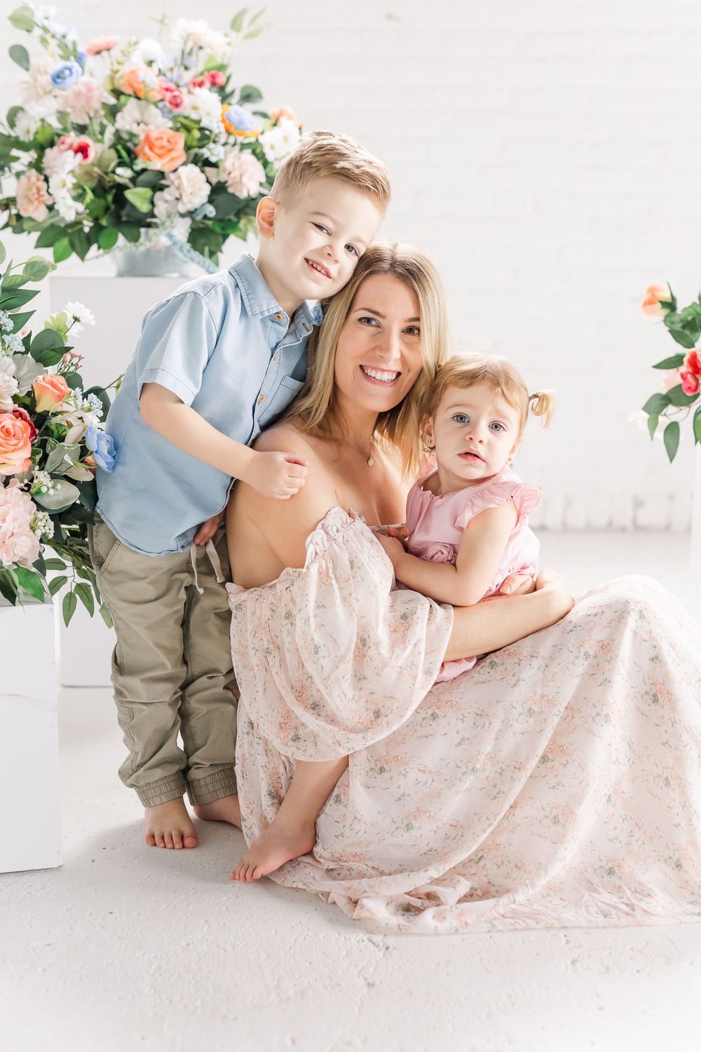 Family portrait in soft pastel colors with floral arrangements against white backdrop.