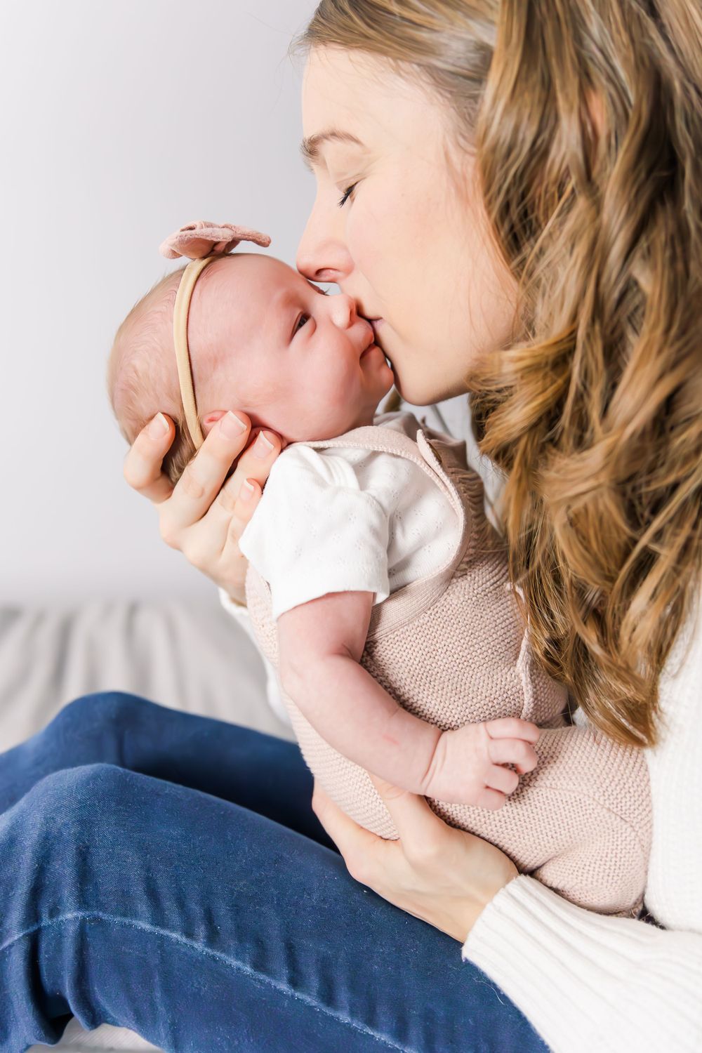 A tender moment between parent and newborn baby sharing a gentle kiss while wearing neutral colored clothing.