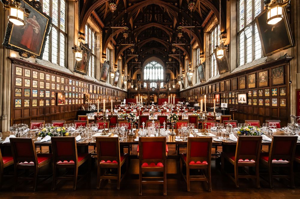 Grand dining hall with wooden beams and red chairs set up for a formal banquet.