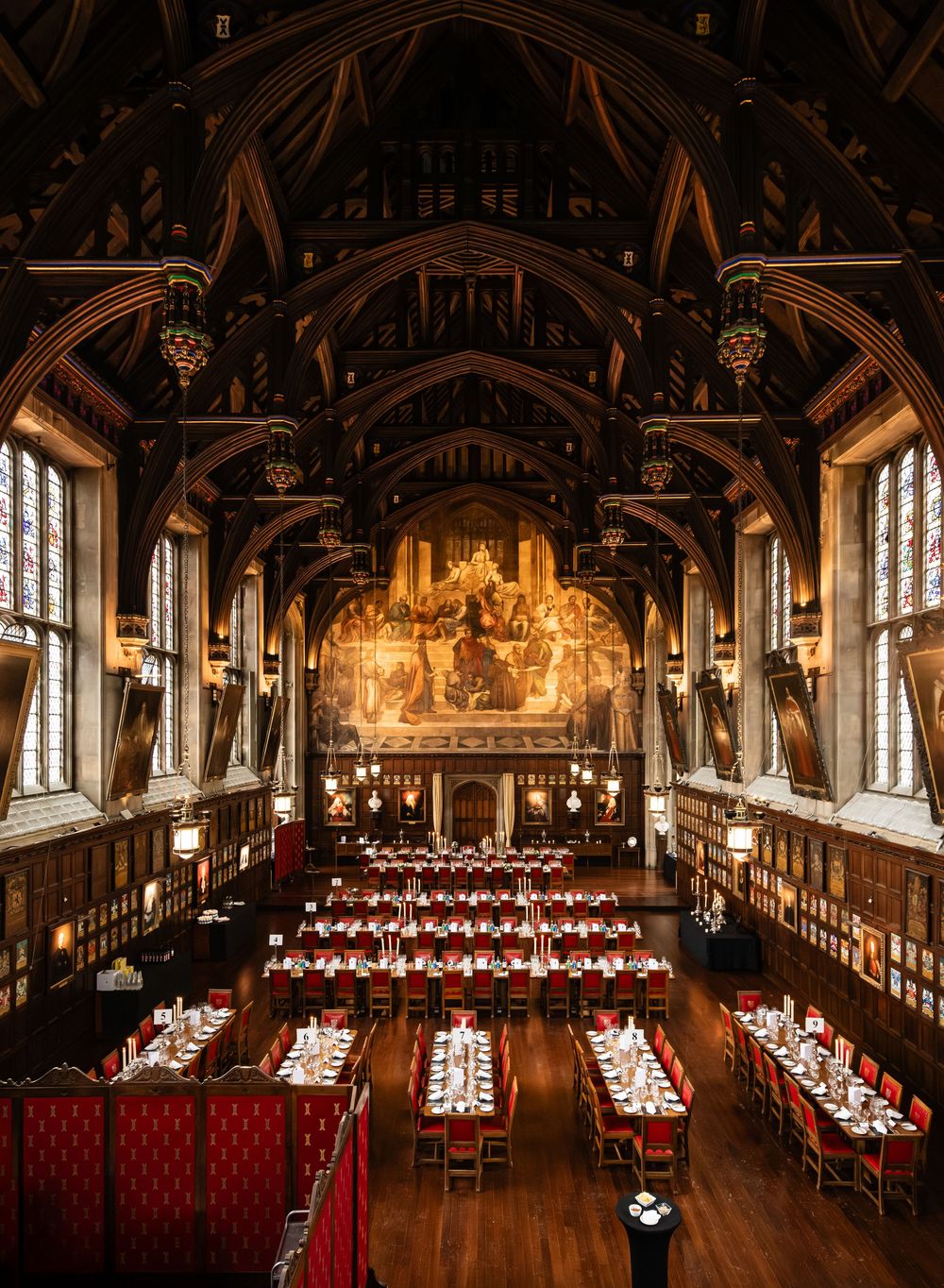 Gothic-style banquet hall with dark wood paneling and red chairs arranged for a formal dinner.