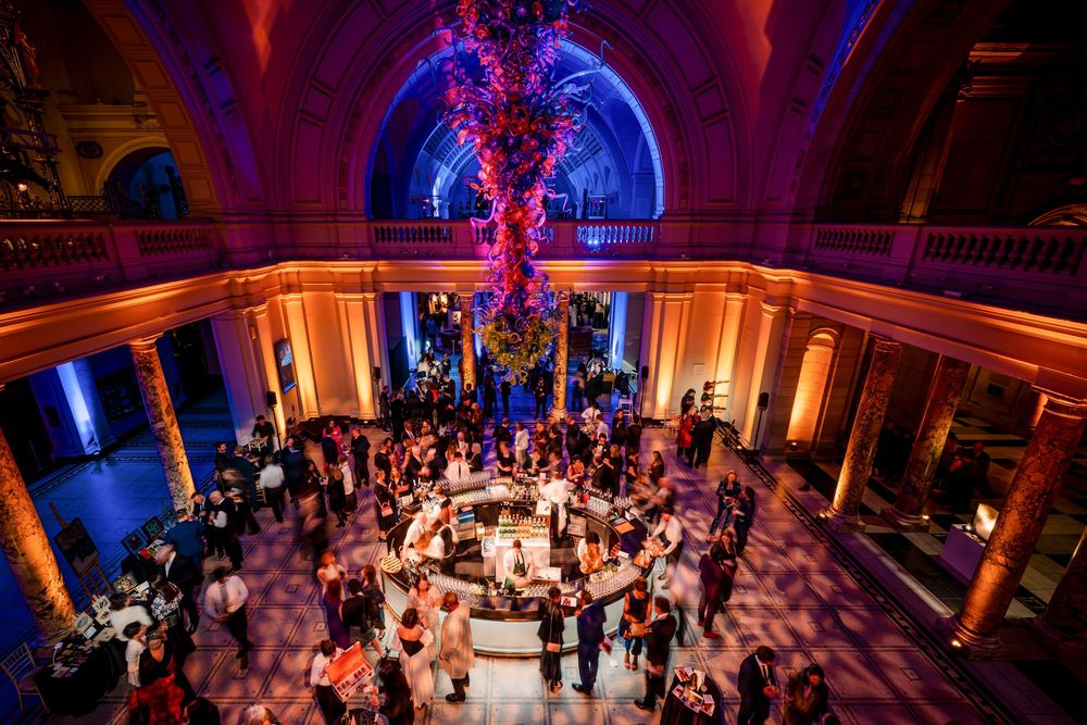 Overhead view of wedding celebration in ornate ballroom with blue uplighting and guests gathered around circular bar.