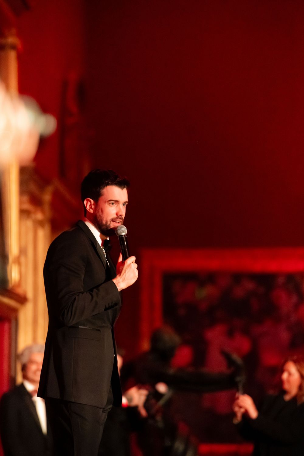 Performer in dark suit on stage under dramatic red spotlighting.