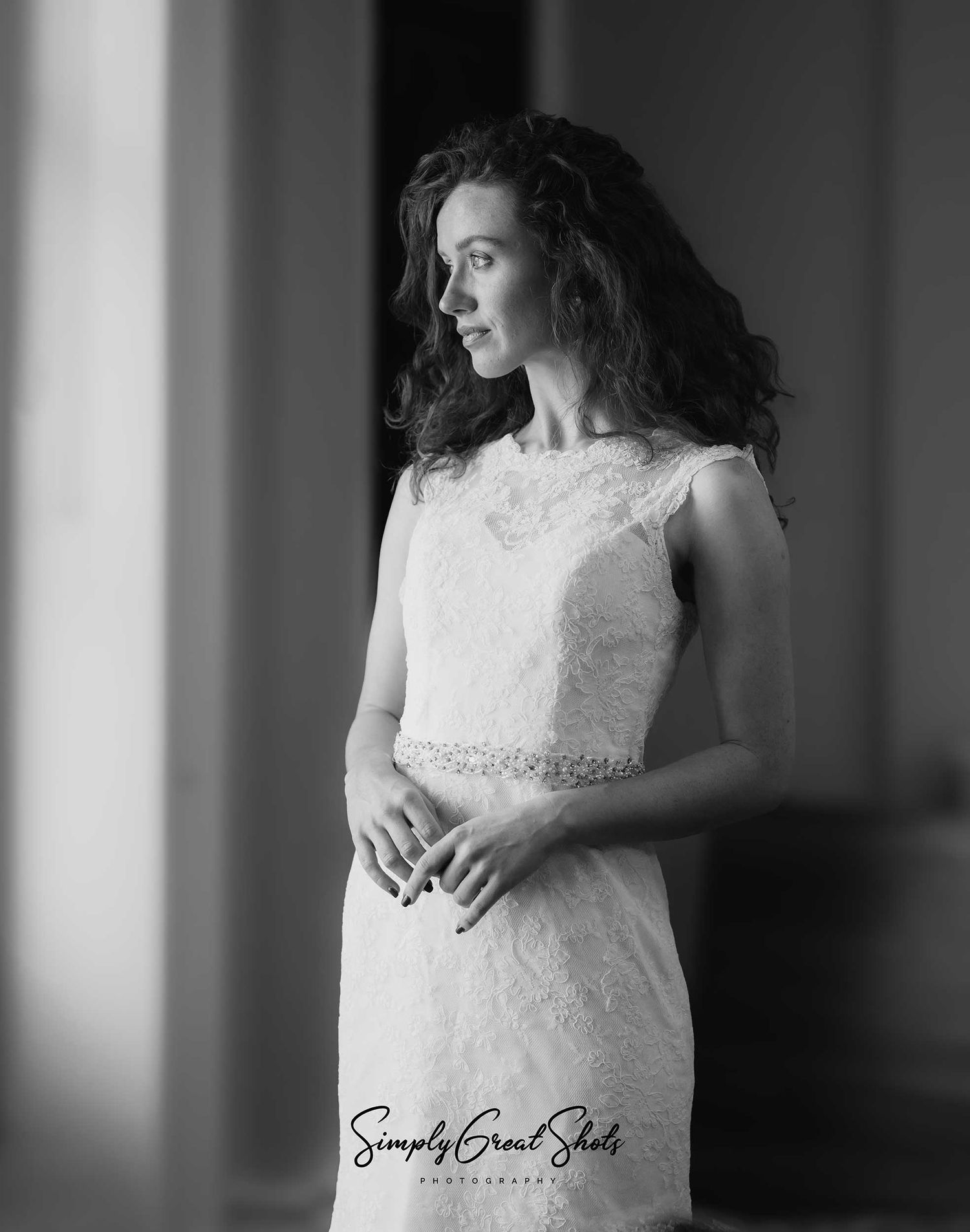 A black and white photograph of a dark-haired lady looking out of a window
