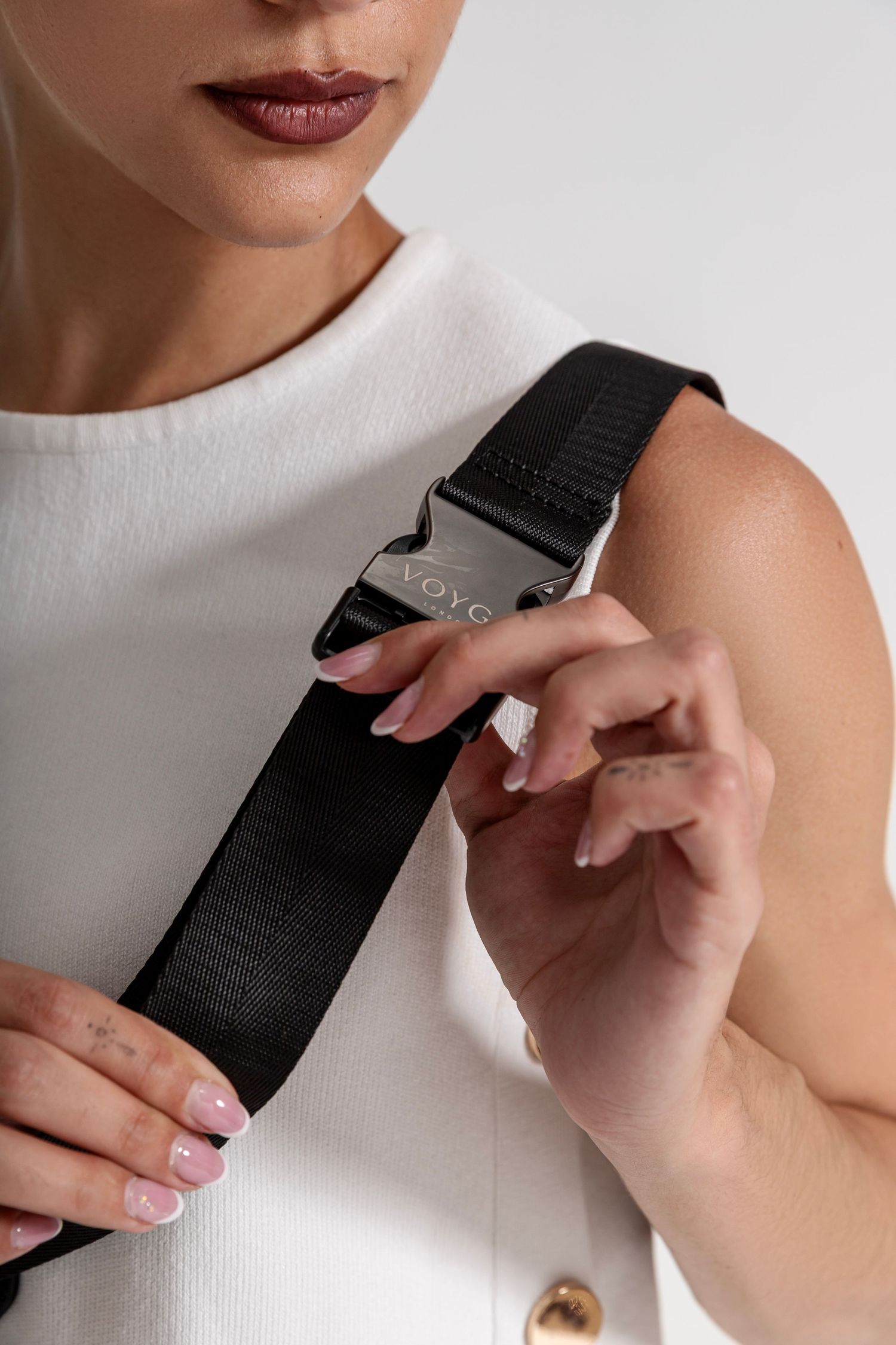 Woman in white top adjusting a black VOYC buckle strap over her shoulder, showcasing the bag accessory.