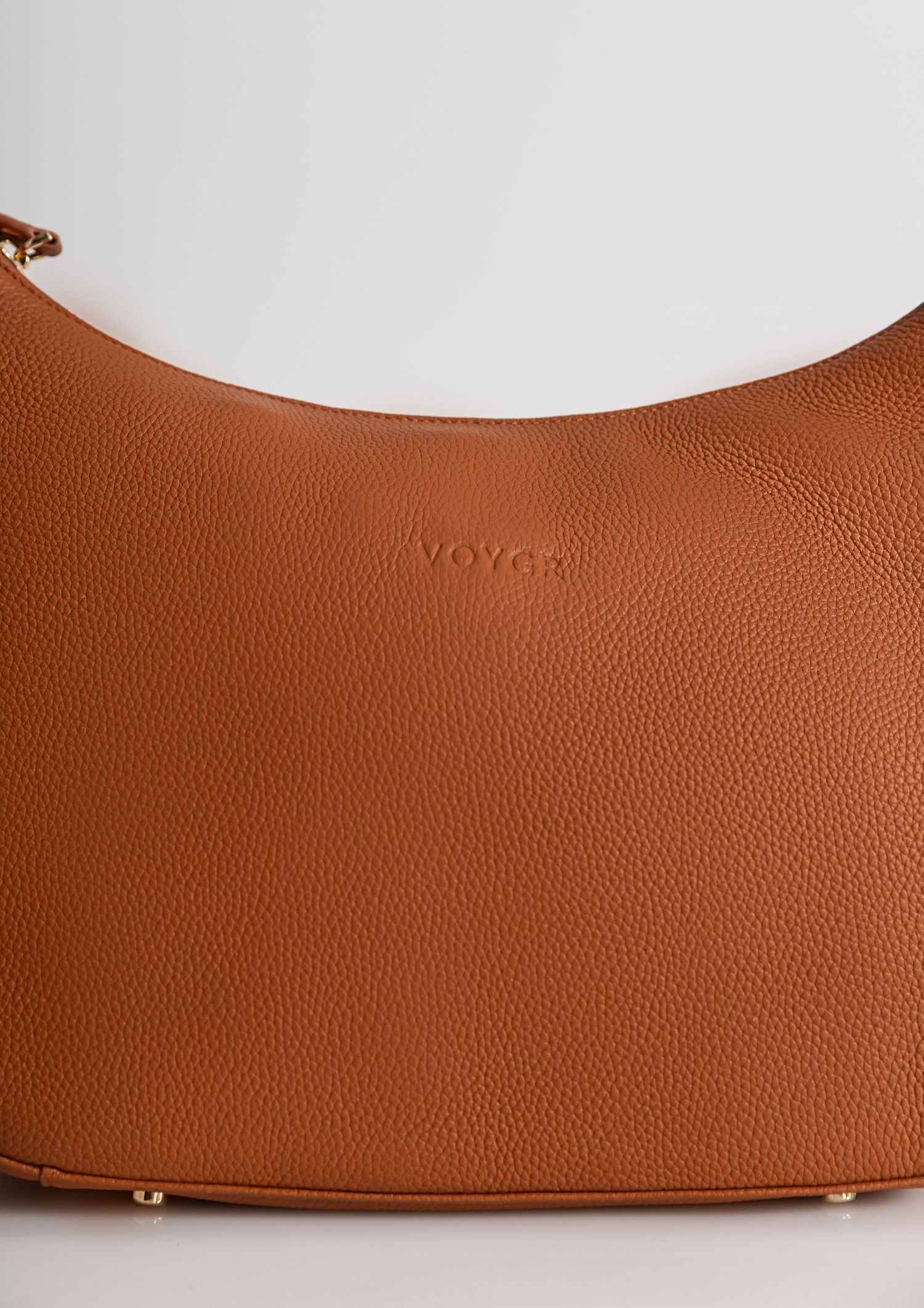 Close-up of a tan pebbled leather Voyen hobo shoulder bag with gold hardware accents.