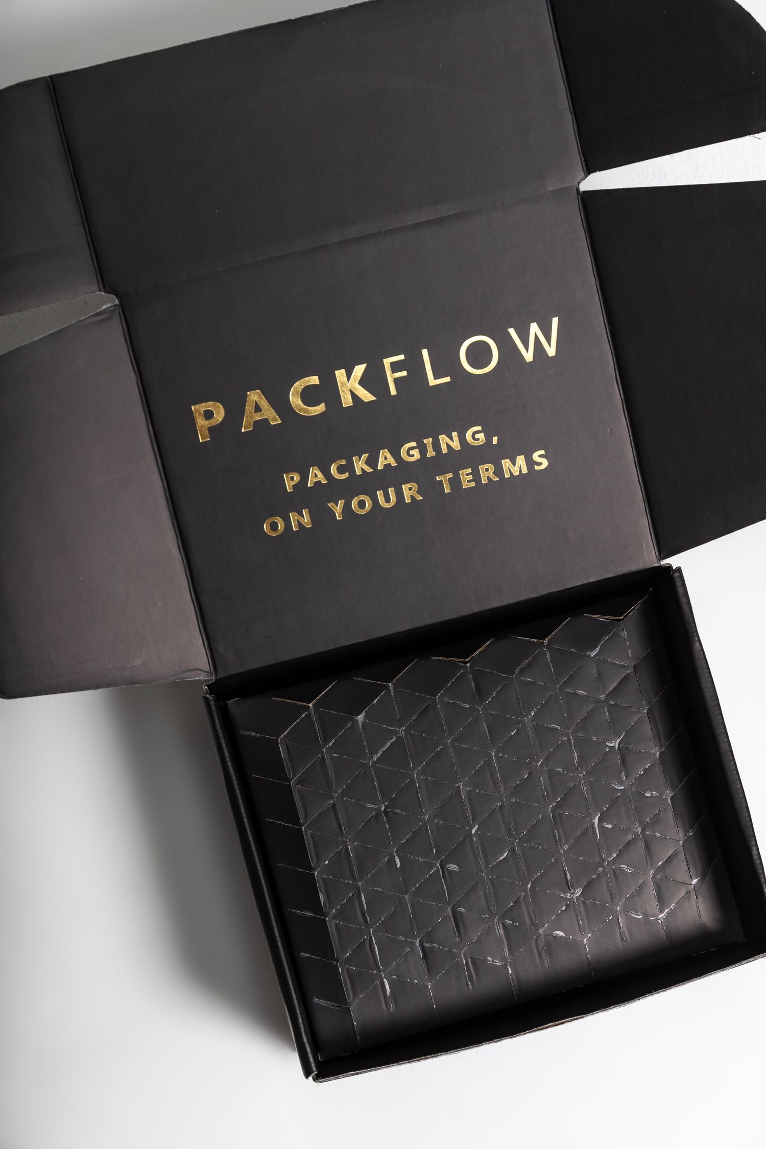 Black luxury gift box with gold foil Packflow branding and geometric textured tissue paper inside.