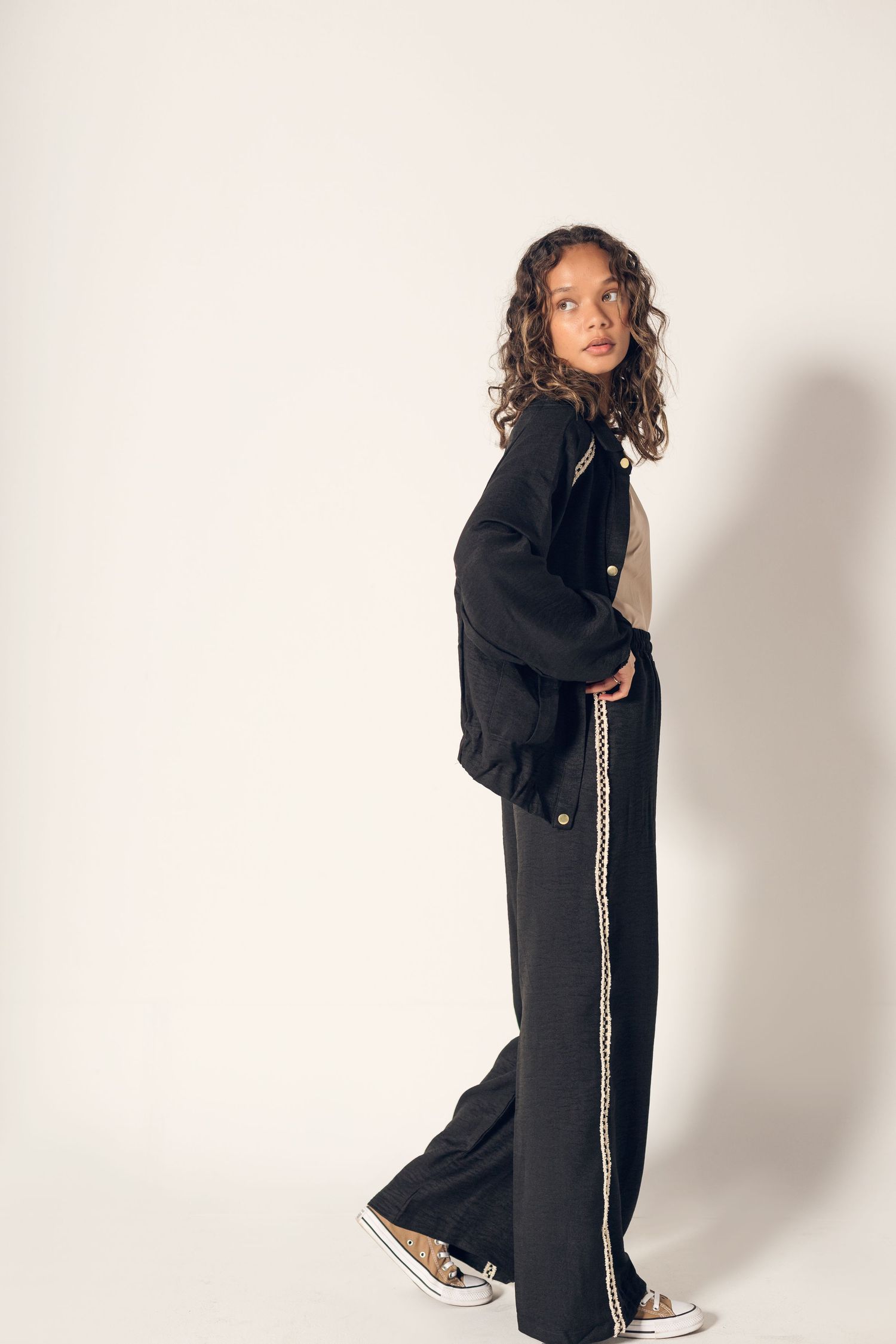 A model in a black oversized coat and sneakers poses against a white background in four different angles.