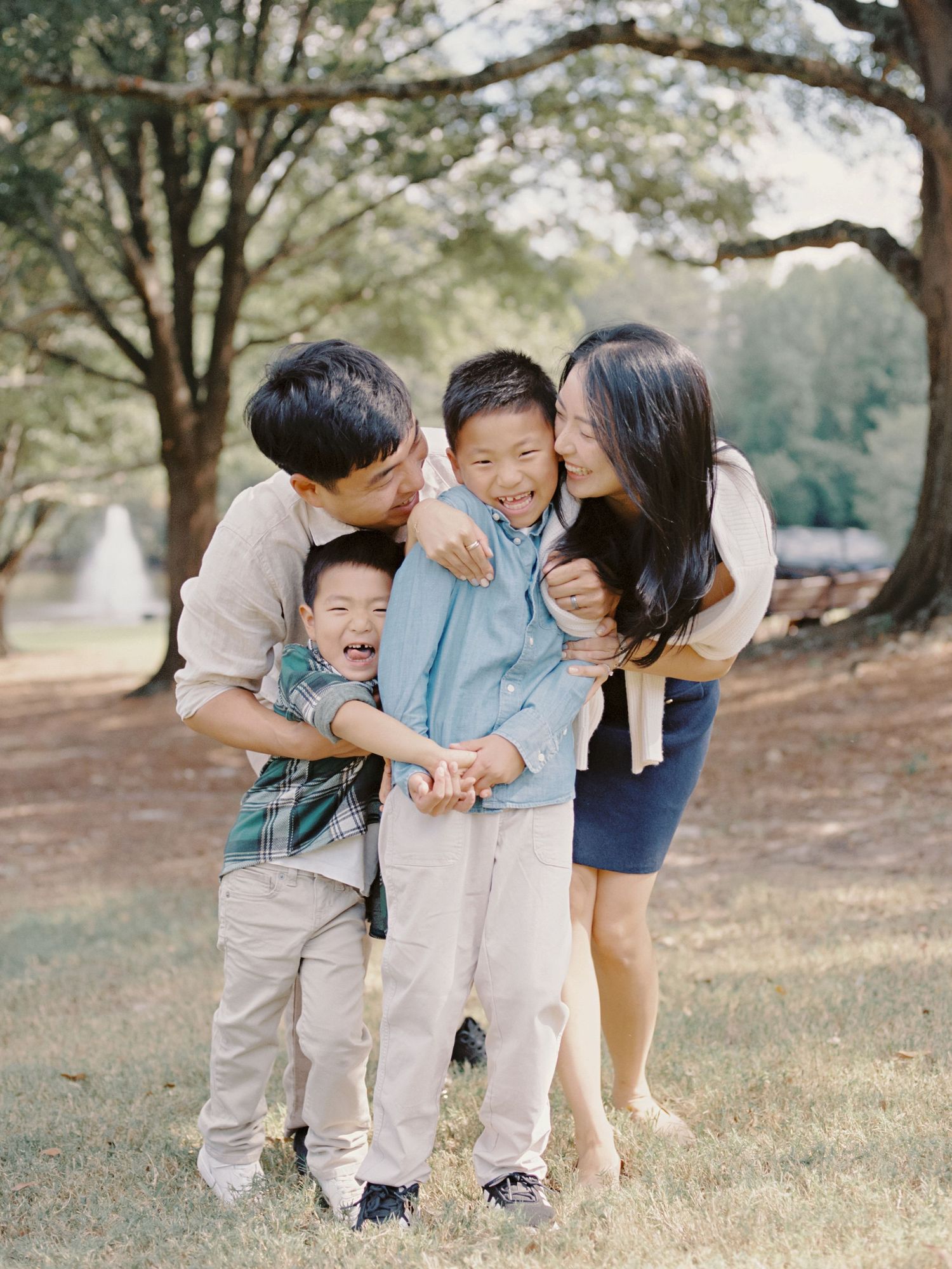 A joyful family moment captured in nature as they share laughter and embrace on a sunny afternoon in the park.