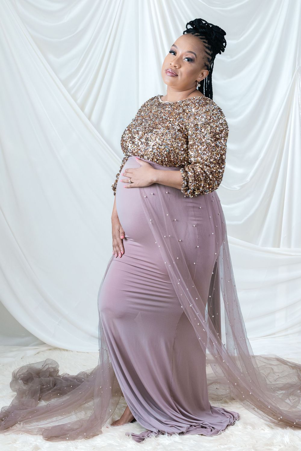 Elegant maternity photo in sparkly top and mauve dress against draped white backdrop.
