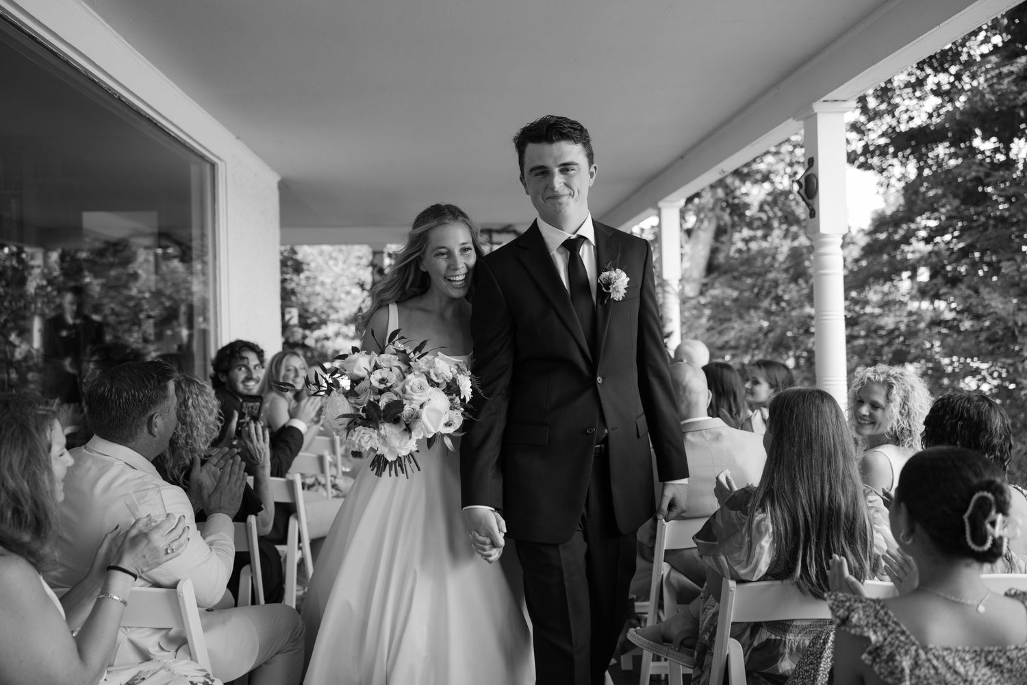 Wedding ceremony on a covered porch with guests seated and watching the celebration.