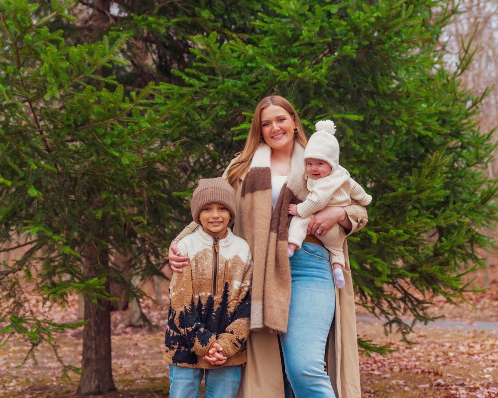 Family enjoying a winter day outdoors by evergreen trees wearing cozy sweaters and warm knit caps.