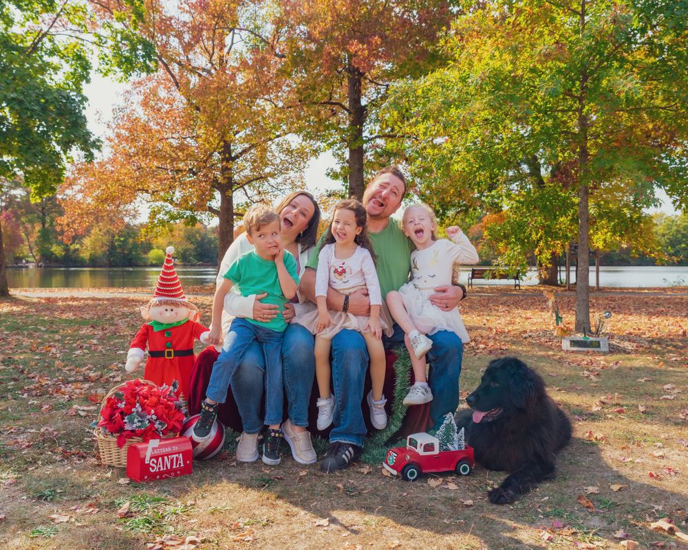 A group sits on Radio Flyer wagons with a black dog under autumn trees in a park setting.