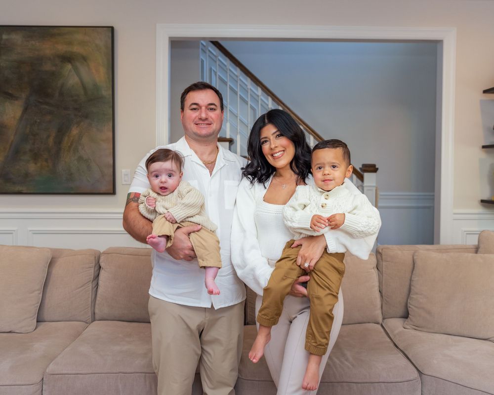 A family group poses together on a beige couch in their modern living room interior.