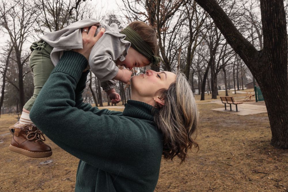 A parent lifts a small child playfully in the air at a park.