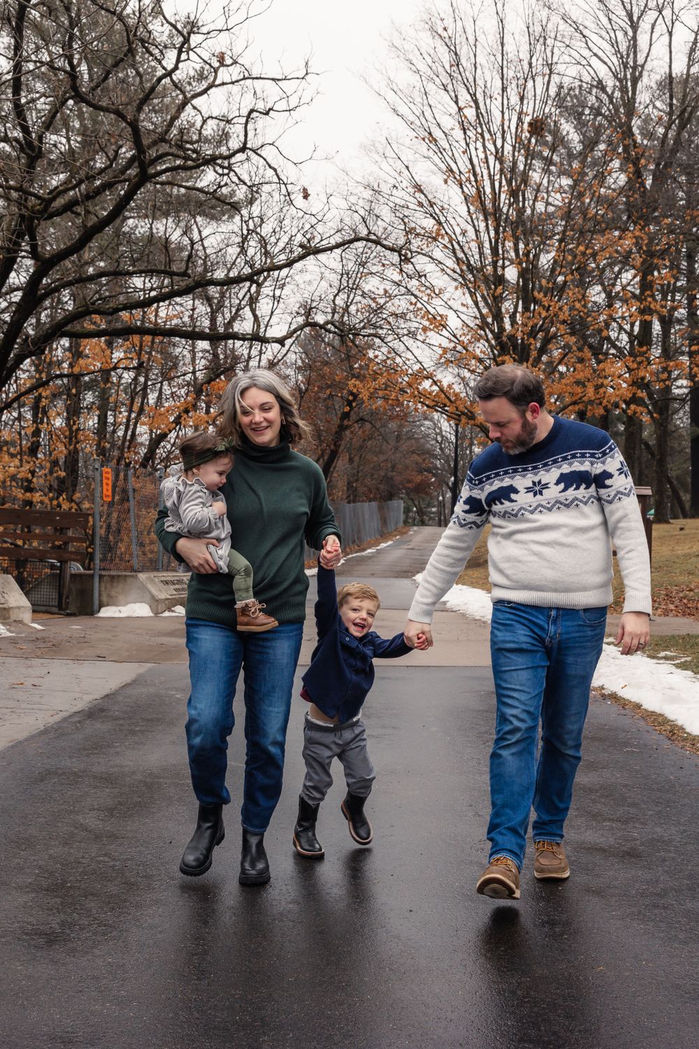 A family walks together on a wet road during autumn with bare trees in background.