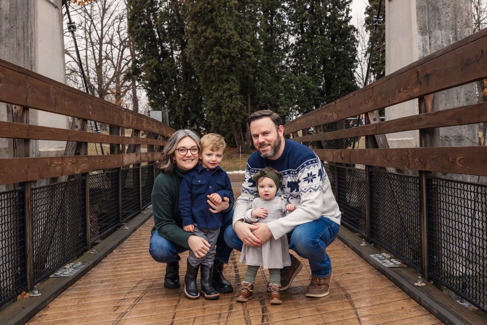 A family poses together on a wooden bridge surrounded by trees.