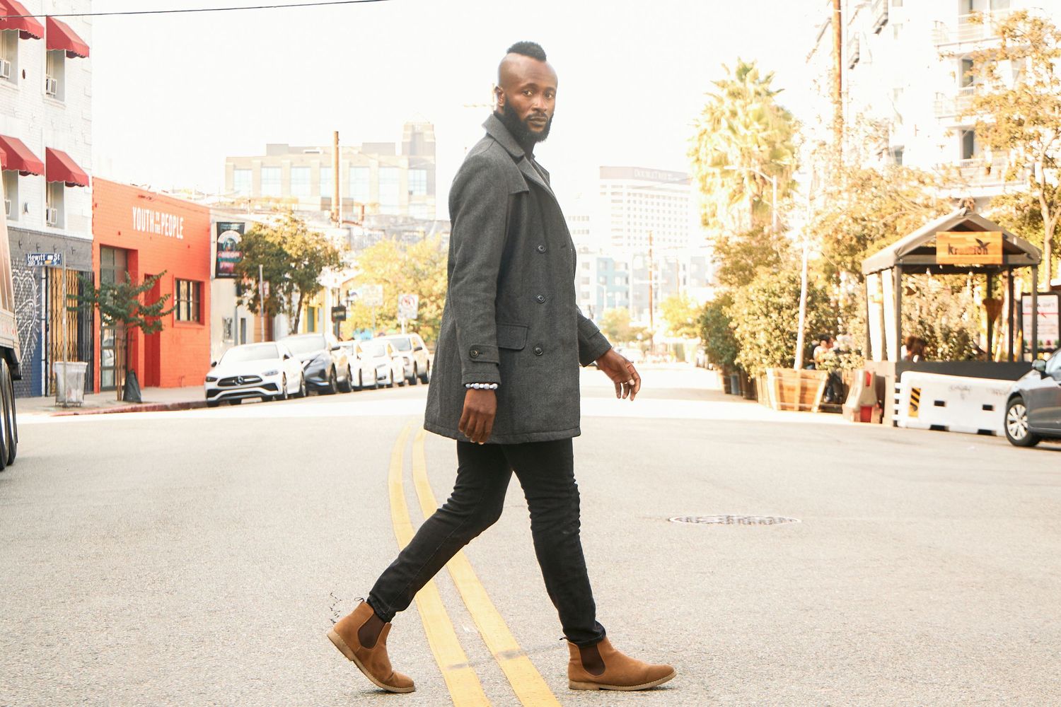 Person walking down urban street wearing grey coat and brown boots.