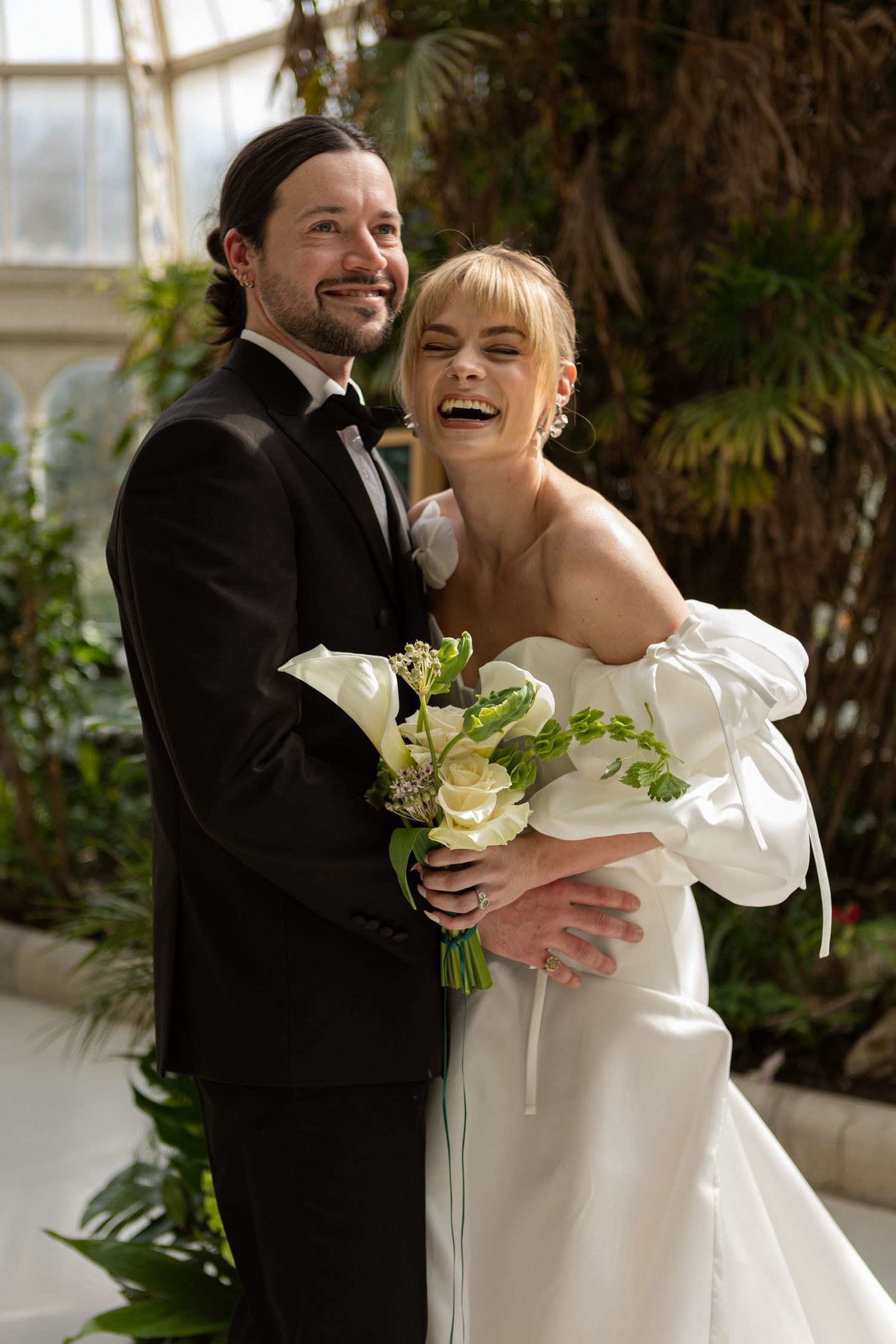 Bride and groom cuddling eachother while bride is laughing holding her wedding bouquet