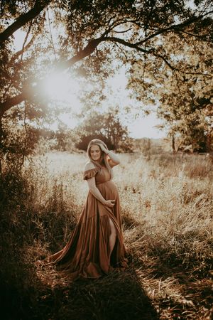Ethereal outdoor photoshoot at sunset with a person in flowing brown dress among trees.
