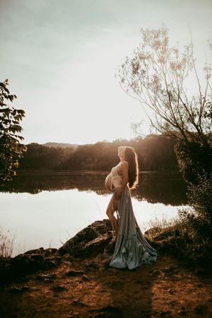 Moody lakeside photoshoot at sunset with flowing dress and dramatic lighting.