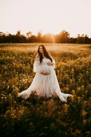 Woman in flowing white dress poses gracefully in a sunlit wildflower meadow at golden hour.
