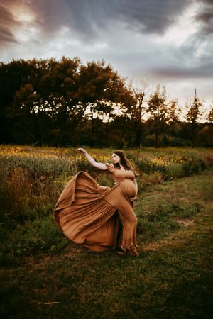 Artistic sunset photoshoot in a field with flowing brown dress and dramatic poses.