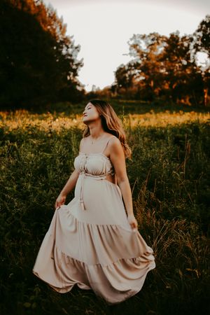 Sunset photoshoot in a meadow featuring flowy beige dress and natural poses.