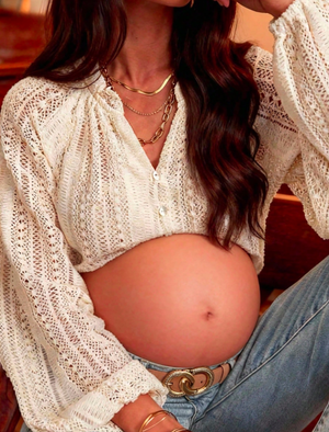 Woman in white crochet top and jeans showing midriff in warm lighting.