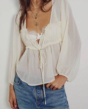 A white sheer peasant blouse with drawstring neckline paired with classic blue denim jeans in a casual style.
