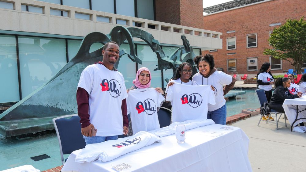 Group of volunteers in white t-shirts staffing tables at an outdoor community event.