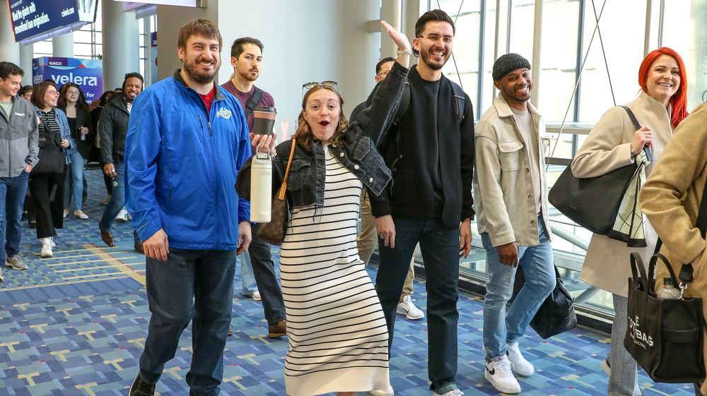 Diverse group of smiling college students walking together through a convention center hallway.
