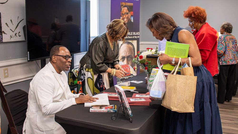 Author signing books at a table during a book signing event with attendees browsing materials nearby.