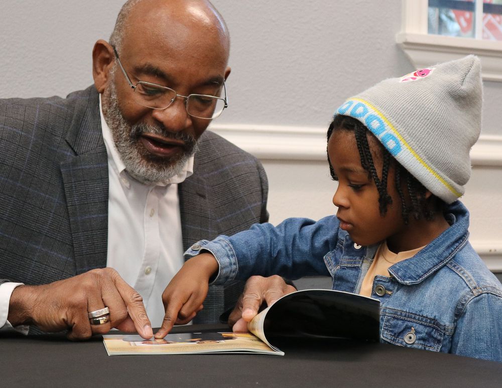 An elderly man and young child reading a picture book together at a table.