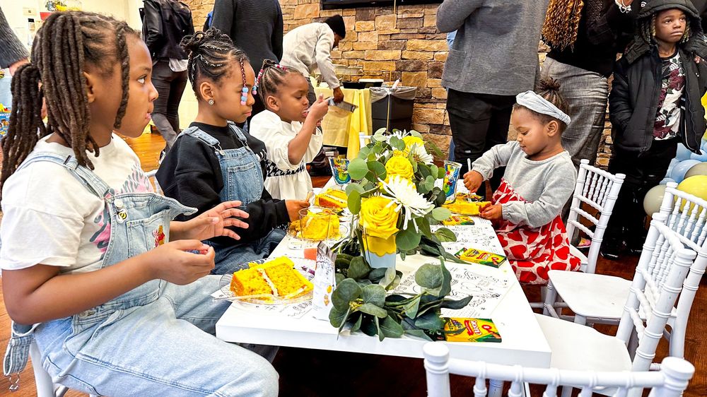 Children enjoy a floral-decorated outdoor table with yellow roses and food at a vibrant kids party celebration.