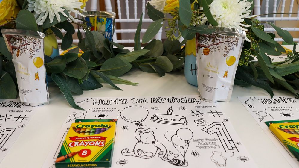 Winnie the Pooh 1st birthday party table with coloring pages, Crayola crayons, and decorated cups with greenery centerpiece.