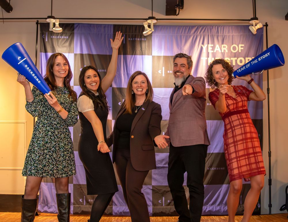 A group of performers on stage wave and smile during what appears to be a theater production finale.