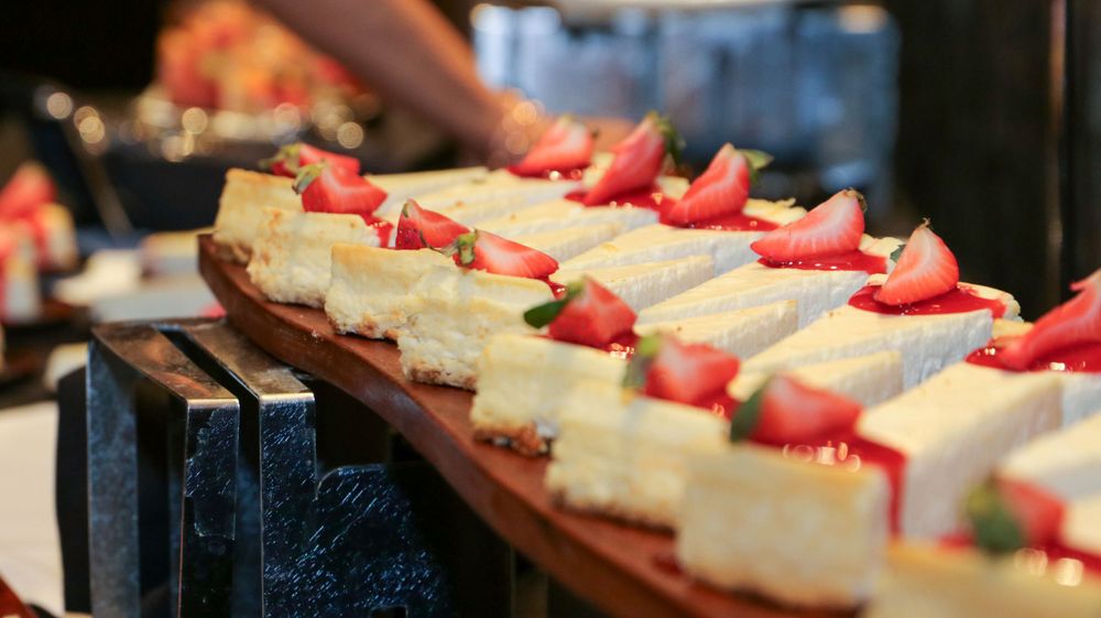 Row of elegant desserts topped with fresh strawberries on a black serving tray.