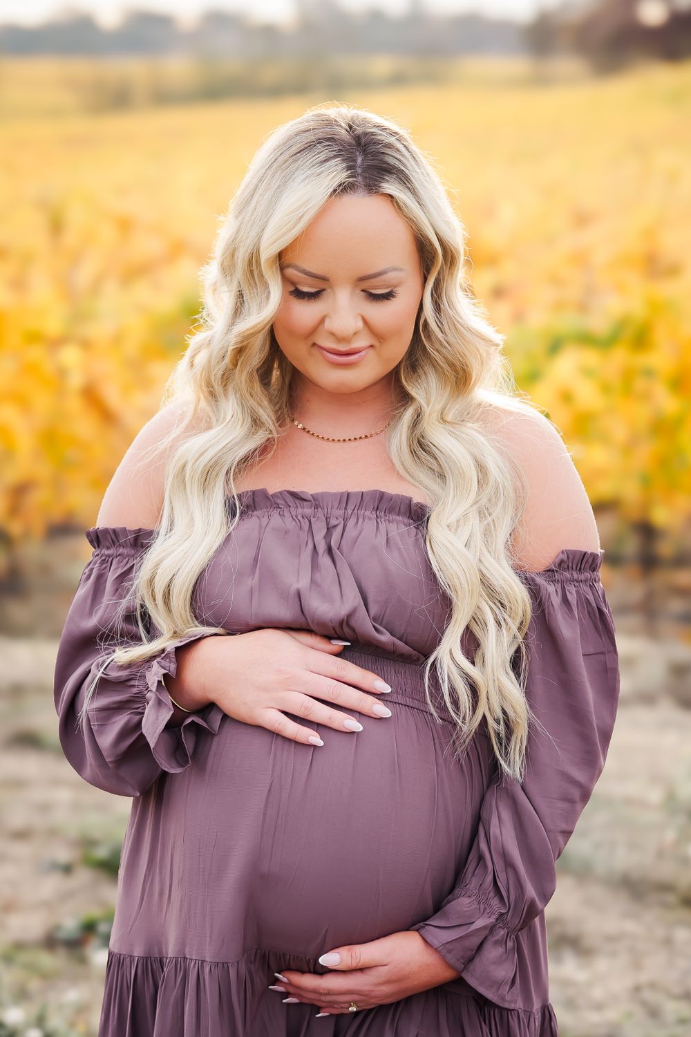 pregnant woman looking down gracefully at her belly in a long flow dress in vineyard in Sonoma County for a maternity session