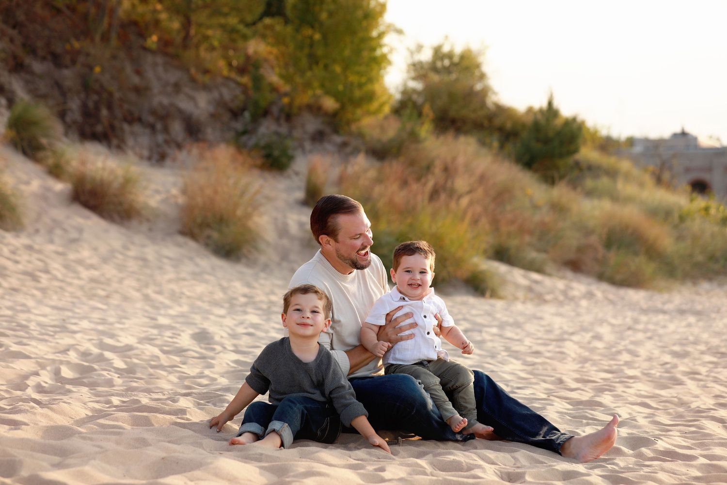 Family beach session enjoying a relaxing afternoon together sitting on sandy dunes at sunset.