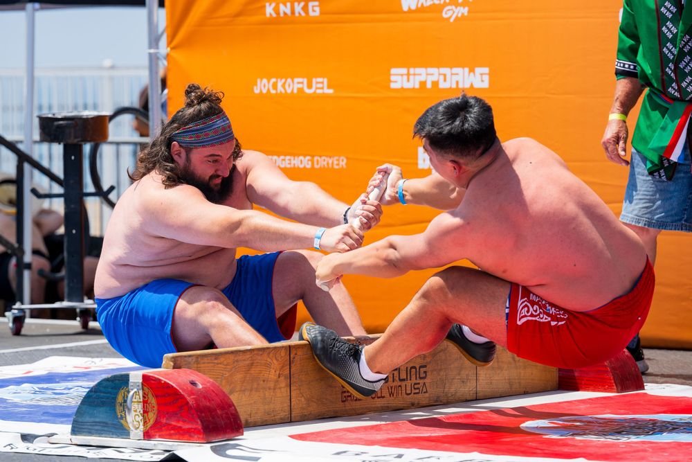 Two shirtless competitors face off in a MAS wrestling match at the Santa Monica Classic with orange banners in background.