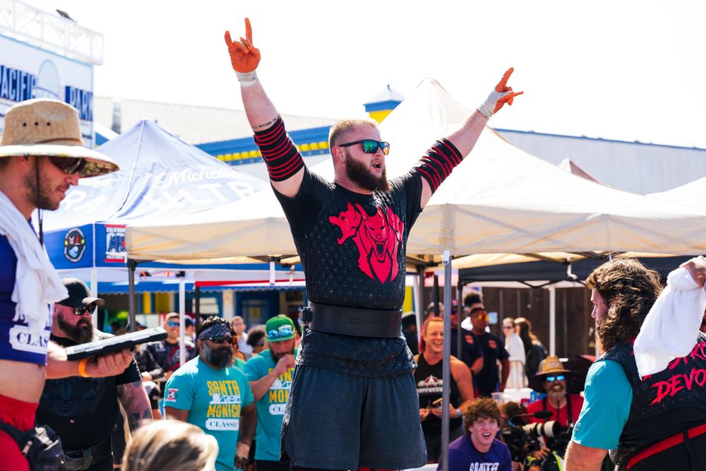 Competitor raises arms victoriously while wearing black shirt at outdoor sporting event.