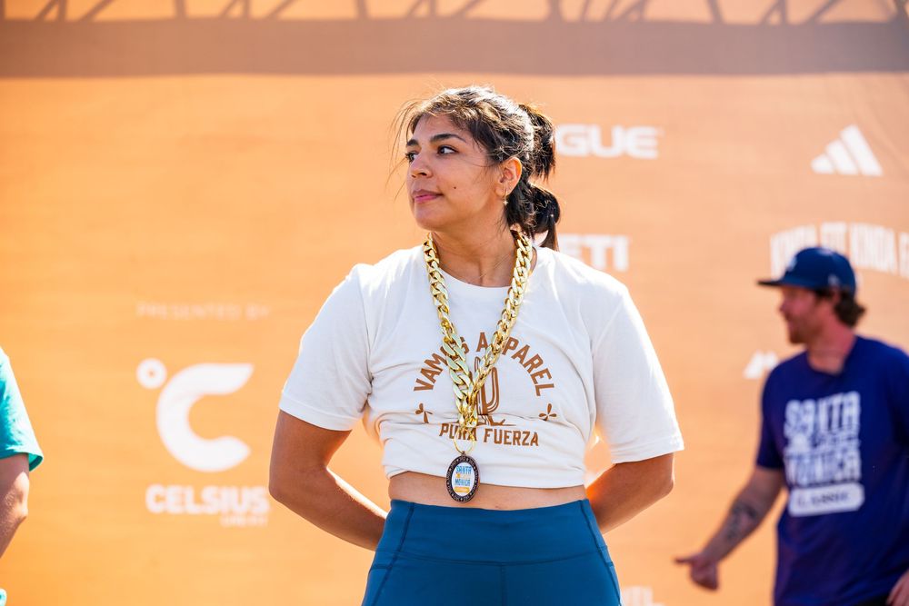 Eve Valdez-Loutherback posing in a white tshirt and blue pants while accepting her medal for the Santa Monica Classic Strongman competition.