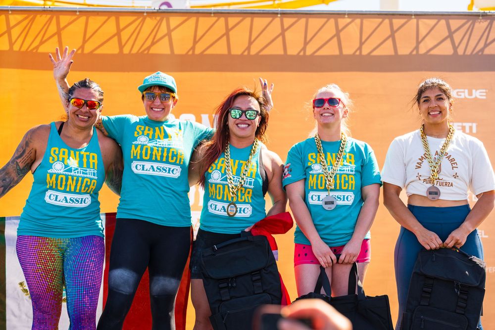 Group of athletic event participants wearing turquoise shirts gather under an orange tent structure.