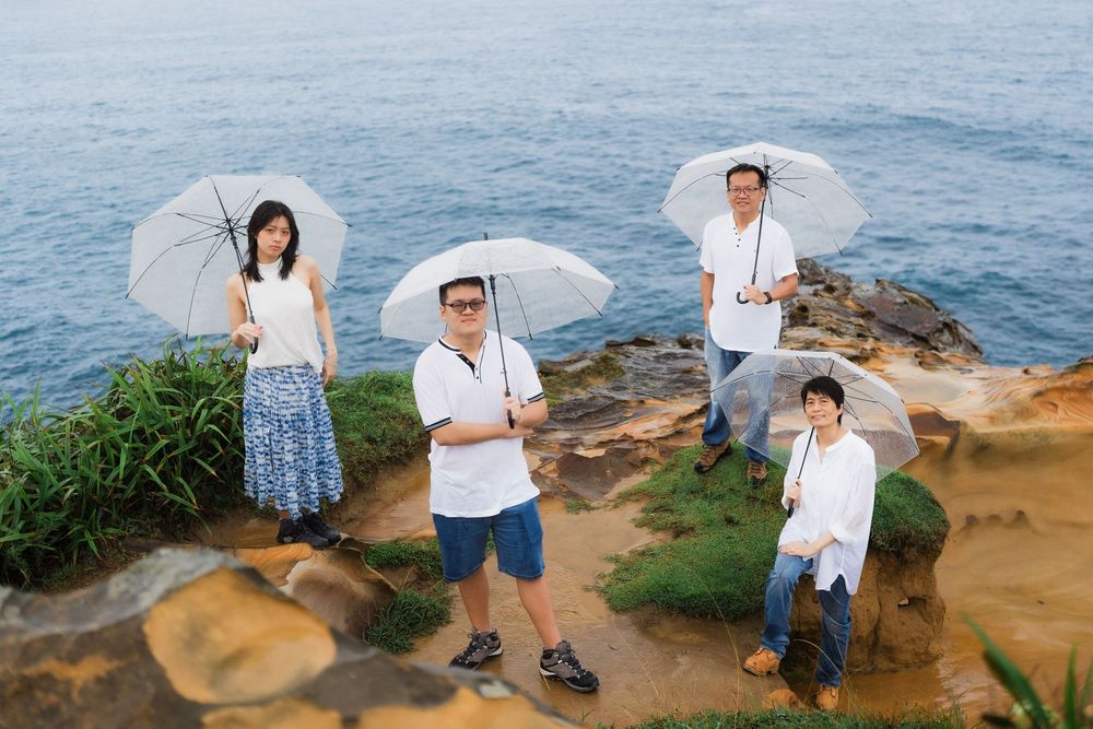 Group of four people holding clear umbrellas on rocky coastal cliff overlooking ocean.
