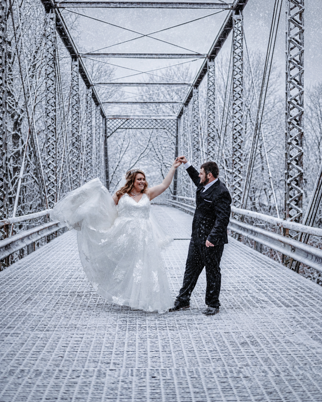 A bride and groom dance on a snow-covered bridge in winter, her white gown flowing as they celebrate their wedding day.