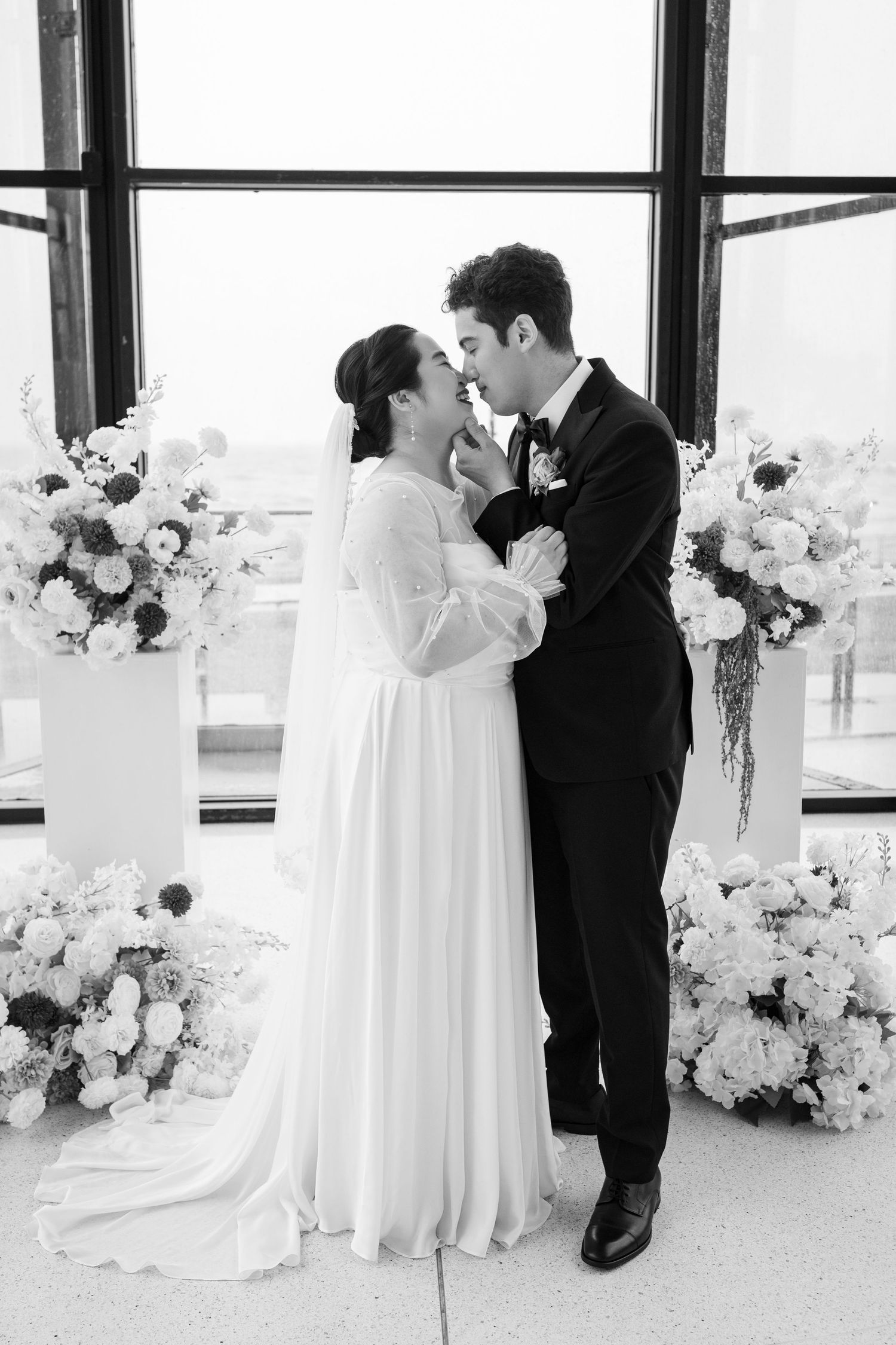 Elegant wedding ceremony in a modern venue with floor-to-ceiling windows, bride and groom exchanging vows before guests.