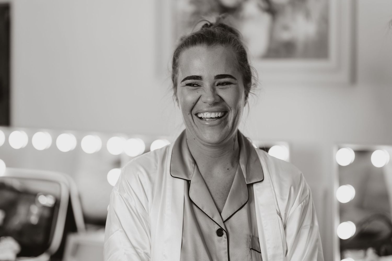 Black and white portrait of a smiling young woman in a white shirt, with bokeh lights in the background.