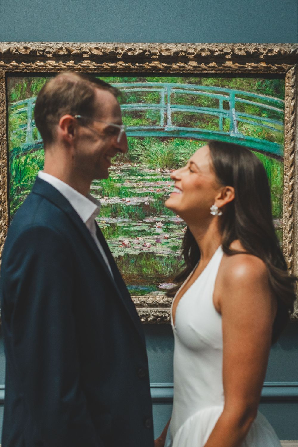 Couple in wedding attire smiling at each other in front of Monet's Water Lilies painting at a museum.